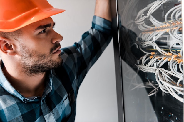 Foto hübscher techniker mit schutzhelm, der drähte und kabel betrachtet