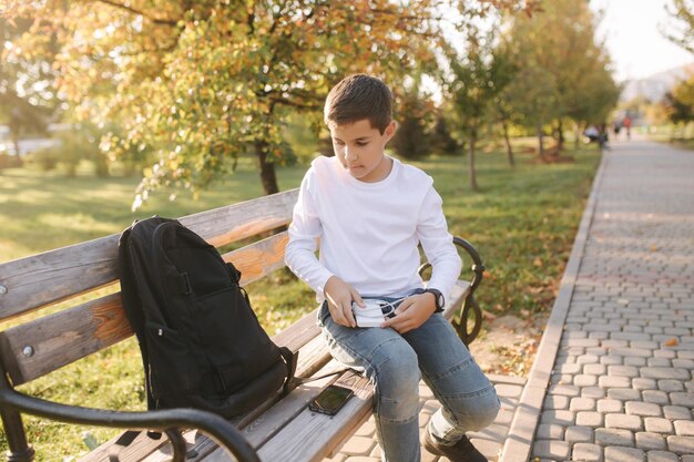 Hübscher Teenager aus seinem Rucksack Powerbark zum Aufladen von Smartphones Süßer Junge im Park im Herbst