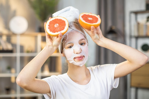 Hübscher Teenager, der Grapefruitscheiben mit Maske im Gesicht hält