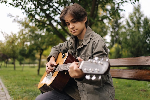 Hübscher Teenager, der im Herbst im Freien Akustikgitarre spielt, der auf einer Bank sitzt und spielt?