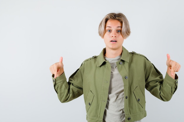 Foto hübscher teenager, der in grüner jacke nach unten zeigt und verwirrt aussieht. vorderansicht.