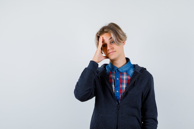 Hübscher Teenager im Hemd, Hoodie, der unter starken Kopfschmerzen leidet und verzweifelt aussieht, Vorderansicht.