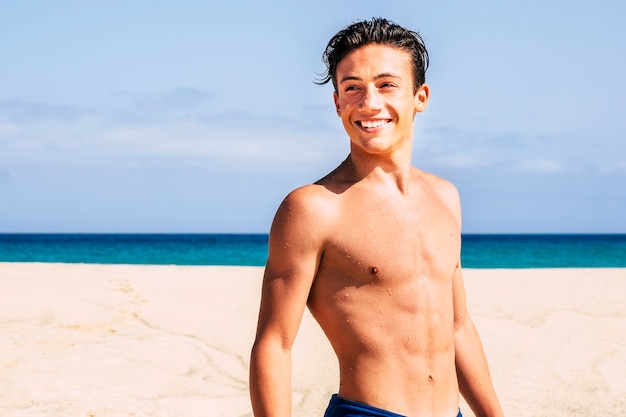 hübscher Teenager Junge am Strand in Badebekleidung, der auf den Rücken schaut und lächelt