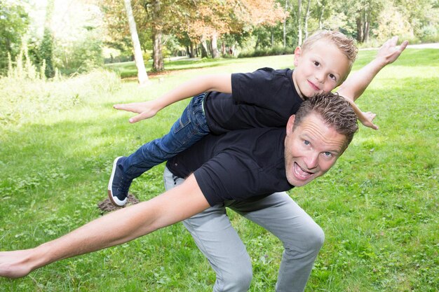 Hübscher Vater und süßer Sohn spielen Spaß im Freien Huckepack-Flugzeug im grünen Gartenhaus