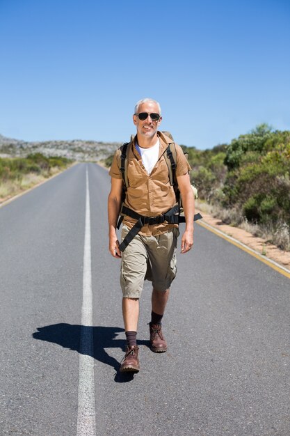 Hübscher Wanderer, der auf Straße geht und an der Kamera lächelt