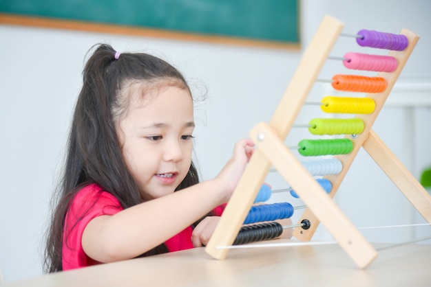 Hübsches asiatisches Mädchen, das Holz auf Abakus in der Schule zählt