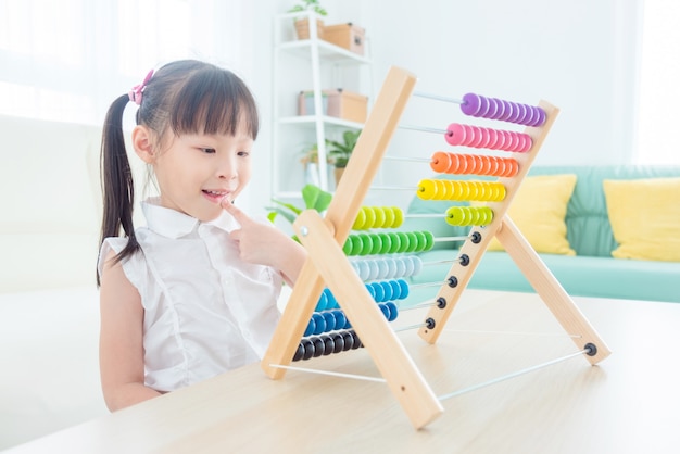 Hübsches asiatisches Mädchen, das zu Hause Holz auf Abakus zählt. Konzept der Kindererziehung.