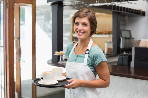 Hübsches barista, das an der Kamera hält Behälter lächelt