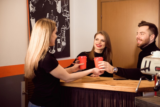 Hübsches barista, das Wegwerfschalen an einer Kaffeestube lächelt und hält