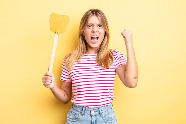 Hübsches blondes Mädchen, das aggressiv mit einem wütenden Ausdruck schreit. Töte Fliegen Konzept