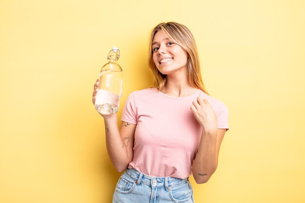 Hübsches blondes Mädchen, das arrogant, erfolgreich, positiv und stolz aussieht. Wasserflaschenkonzept