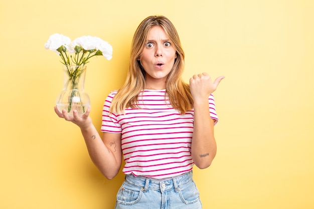 Hübsches blondes Mädchen, das erstaunt ungläubig aussieht. dekoratives blumenkonzept