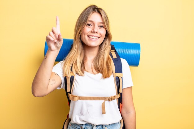 Hübsches blondes Mädchen, das freundlich lächelt und aussieht und Nummer eins zeigt. Wanderer-Konzept