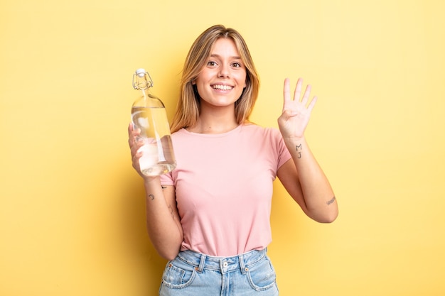 Hübsches blondes Mädchen, das freundlich lächelt und aussieht und Nummer vier zeigt. Wasserflaschenkonzept