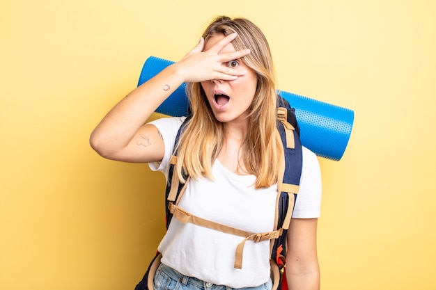 Hübsches blondes Mädchen, das schockiert, verängstigt oder verängstigt aussieht und das Gesicht mit der Hand bedeckt. Wanderer-Konzept