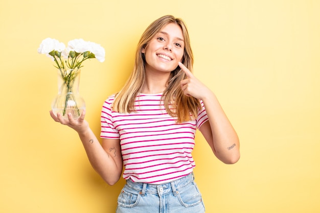 Hübsches blondes Mädchen, das selbstbewusst lächelt und auf ein breites Lächeln zeigt. dekoratives Blumenkonzept