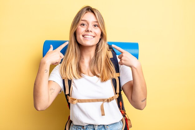 Hübsches blondes Mädchen, das selbstbewusst lächelt und auf ein breites Lächeln zeigt. Wanderer-Konzept