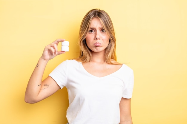 Hübsches blondes Mädchen, das sich traurig und weinerlich mit einem unglücklichen Blick und Weinen fühlt. Pillenflaschenkonzept