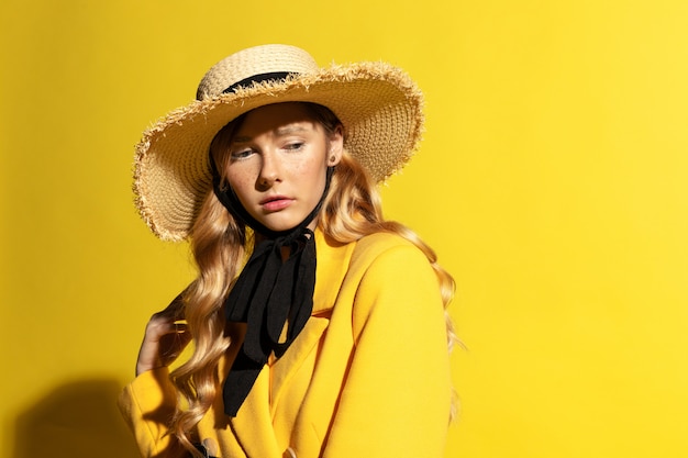 Hübsches blondes Mädchen mit Sommersprossen im gelben Outfit und Strohhut auf Gelb