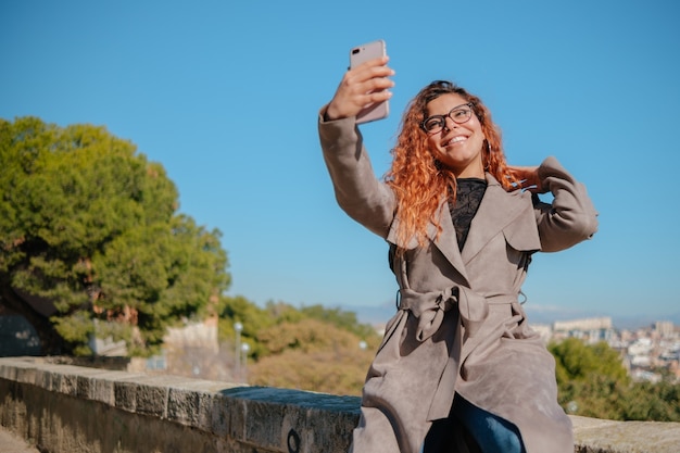 Hübsches brünettes Latina-Mädchen, das ein Selbstporträt mit ihrem Handy draußen macht