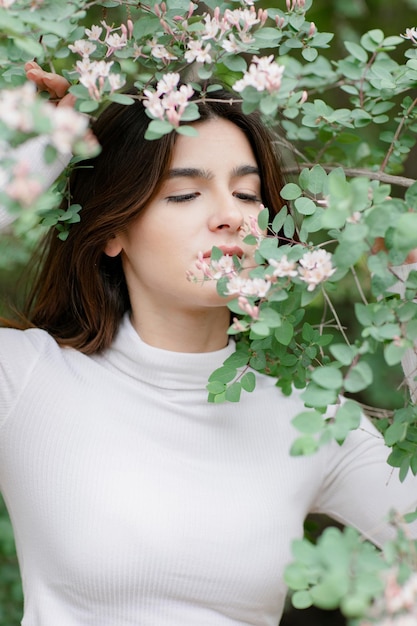 Hübsches brünettes Mädchen mit Fotoshooting im Park, riechender Baumzweig, der nach unten schaut