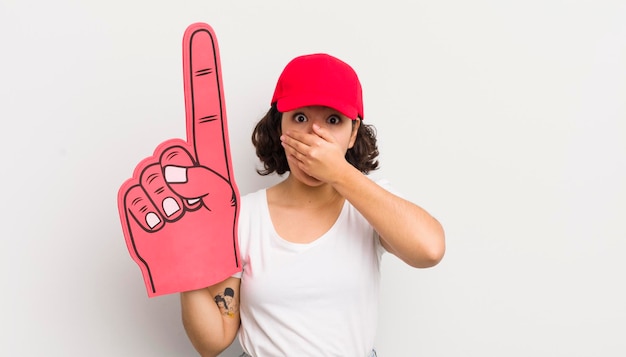 Hübsches hispanisches Mädchen, das den Mund mit den Händen bedeckt, mit einem schockierten Handfan-Konzept Nummer eins