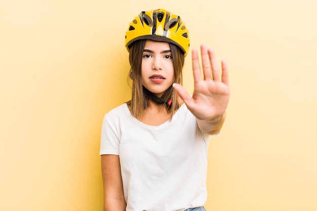 Hübsches hispanisches Mädchen, das ernsthaft aussieht und eine offene Handfläche zeigt, die ein Stoppgesten-Fahrradkonzept macht