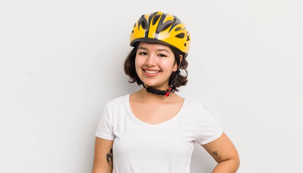 Hübsches hispanisches Mädchen, das glücklich mit einer Hand auf Hüfte und selbstbewusstem Fahrradkonzept lächelt