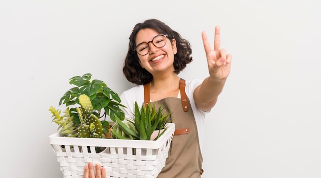 Hübsches hispanisches Mädchen, das lächelt und glücklich aussieht, gestikuliert den Sieg oder das Konzept der Friedenspflanzen