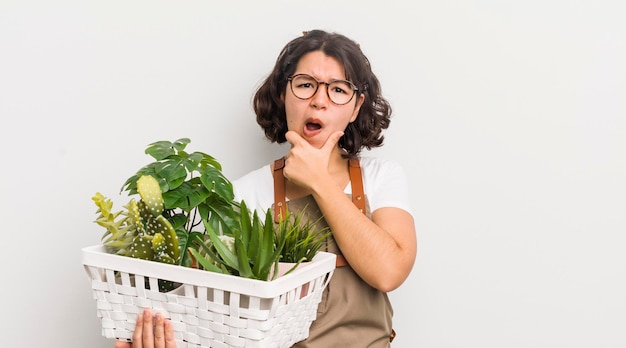 Hübsches hispanisches Mädchen mit weit geöffnetem Mund und Augen und Hand auf dem Konzept der Kinnpflanzen