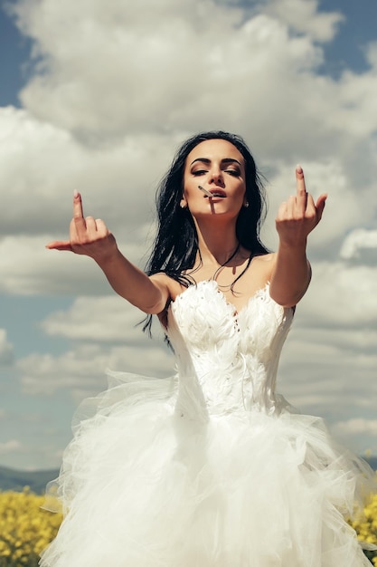 Hübsches Hochzeitsmädchen am blauen Himmel mit Mittelfinger