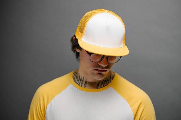 Hübsches hübsches männliches Modell des Hipsters, das gelbe leere Baseballkappe mit Platz für Ihr Logo über grauem Hintergrund trägt