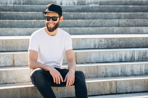 Hübsches hübsches männliches Modell des Hipsters mit Bart, das weißes leeres T-Shirt mit Platz für Ihr Logo oder Design im lässigen urbanen Stil trägt
