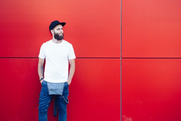 Hübsches hübsches männliches Modell des Hipsters mit Bart, der weißes leeres T-Shirt und eine Baseballkappe mit Platz für Ihr Logo trägt