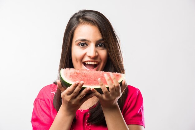 Hübsches indisches oder asiatisches Mädchen, das eine Scheibe Wassermelone oder Tarbuja in Hindi hält und lokalisiert über weißem oder gelbem Hintergrund steht.