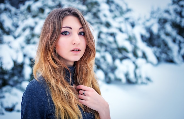 Hübsches junges Mädchen, das im Winter im kalten Wald mit Kiefern aufwirft.