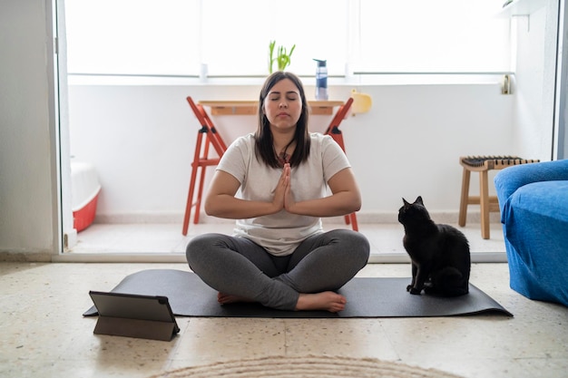 hübsches junges mädchen, das in ihrem wohnzimmer mit einer schwarzen katze übungen und yoga praktiziert