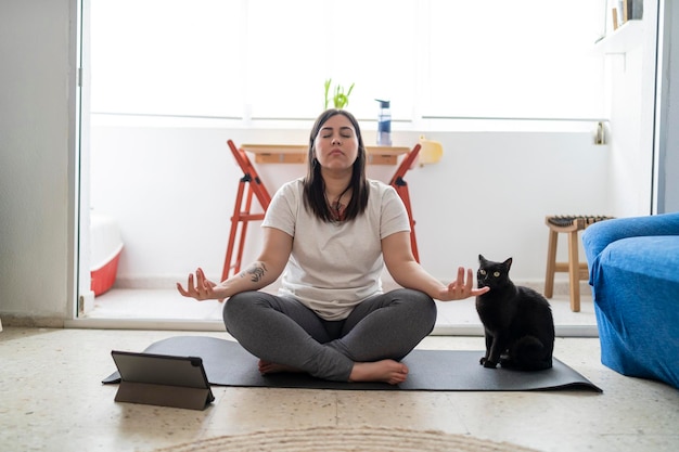 Foto hübsches junges mädchen, das in ihrem wohnzimmer mit einer schwarzen katze übungen und yoga praktiziert