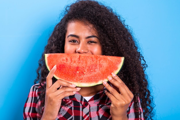 Hübsches junges Mädchen, das Scheibe Wassermelone vor ihrem Gesicht hält. Porträt des lächelnden Afroamerikanermädchens lokalisiert gesund & glücklich