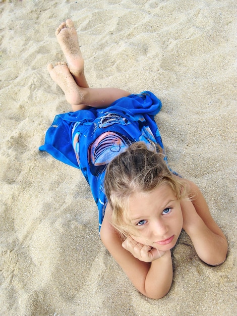 Hübsches junges Mädchen im blauen Pareo liegt am Strand und schaut nach oben.