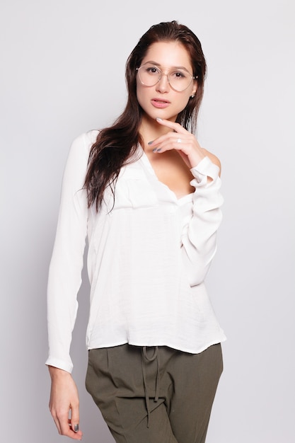 Hübsches junges Mädchen im weißen leeren T-Shirt, Brille tragend, leere Wand, Studioporträt