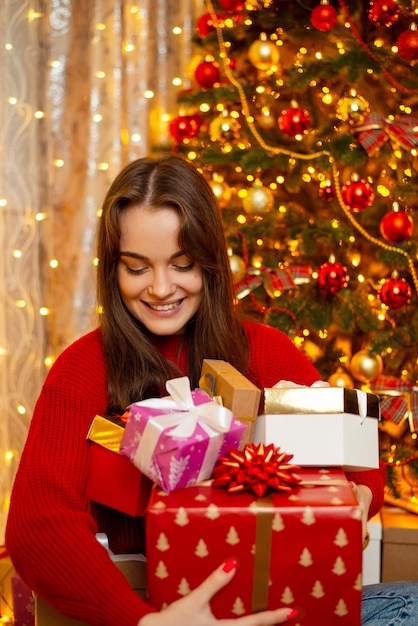 Hübsches junges Mädchen in leuchtend rotem Pullover mit vielen Geschenken am Weihnachtsmorgen