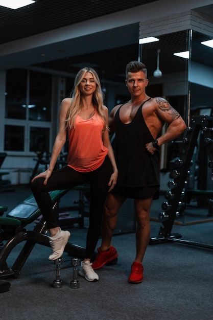 Hübsches junges schlankes Mädchen und ein sportlicher gutaussehender Mann mit einem muskulösen Körper mit einem Tattoo-Zug im Fitnessstudio. Schönes Sportpaar und gesunder Lebensstil