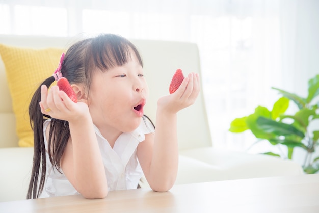 Hübsches kleines asiatisches Mädchen, das zu Hause Erdbeere isst. Gesundes Essen und Kinderkonzept.