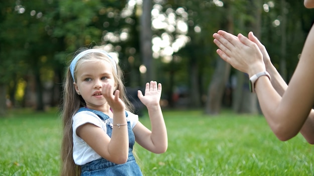 Hübsches kleines Kindermädchen, das mit ihrer Mutter mit ihren Händen draußen im grünen Sommerpark Spiel spielt.