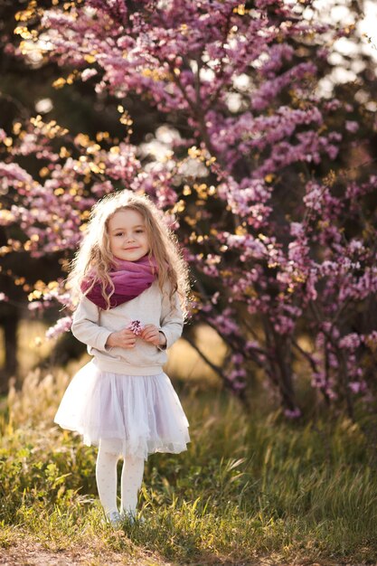 Hübsches kleines Kindermädchen mit Blumen über blühendem Naturhintergrund