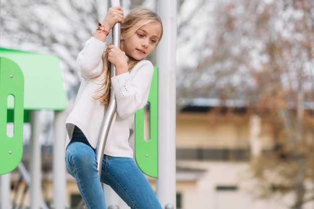 Hübsches, kleines Mädchen, das auf dem Kinderspielplatz, bereit spielt, durch Pfosten zu schieben.