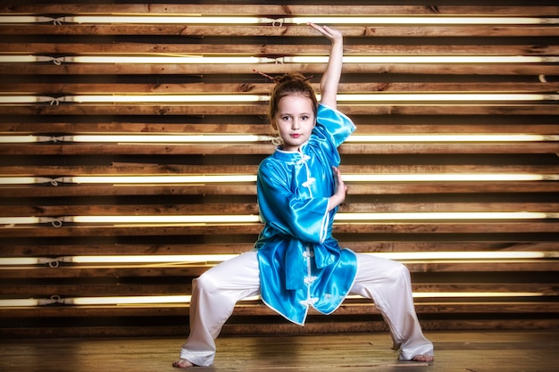 Hübsches kleines Mädchen im Raum in Sportbekleidung für Kampfsportarten ist Wushu oder Kung Fu