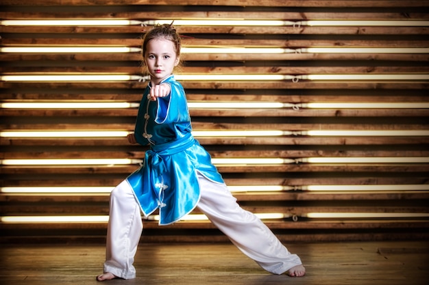 Hübsches kleines Mädchen im Raum in Sportbekleidung für Kampfsportarten ist Wushu oder Kung Fu
