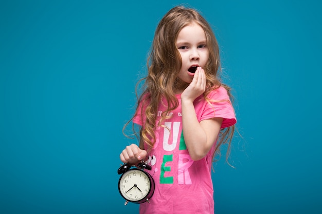 Hübsches, kleines Mädchen im T-Shirt mit dem brünetten Haar, mit Uhr in den Händen